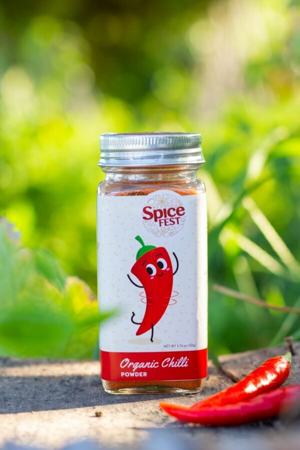 Close-up of organic chilli powder in a labeled jar with fresh peppers, outdoors.
